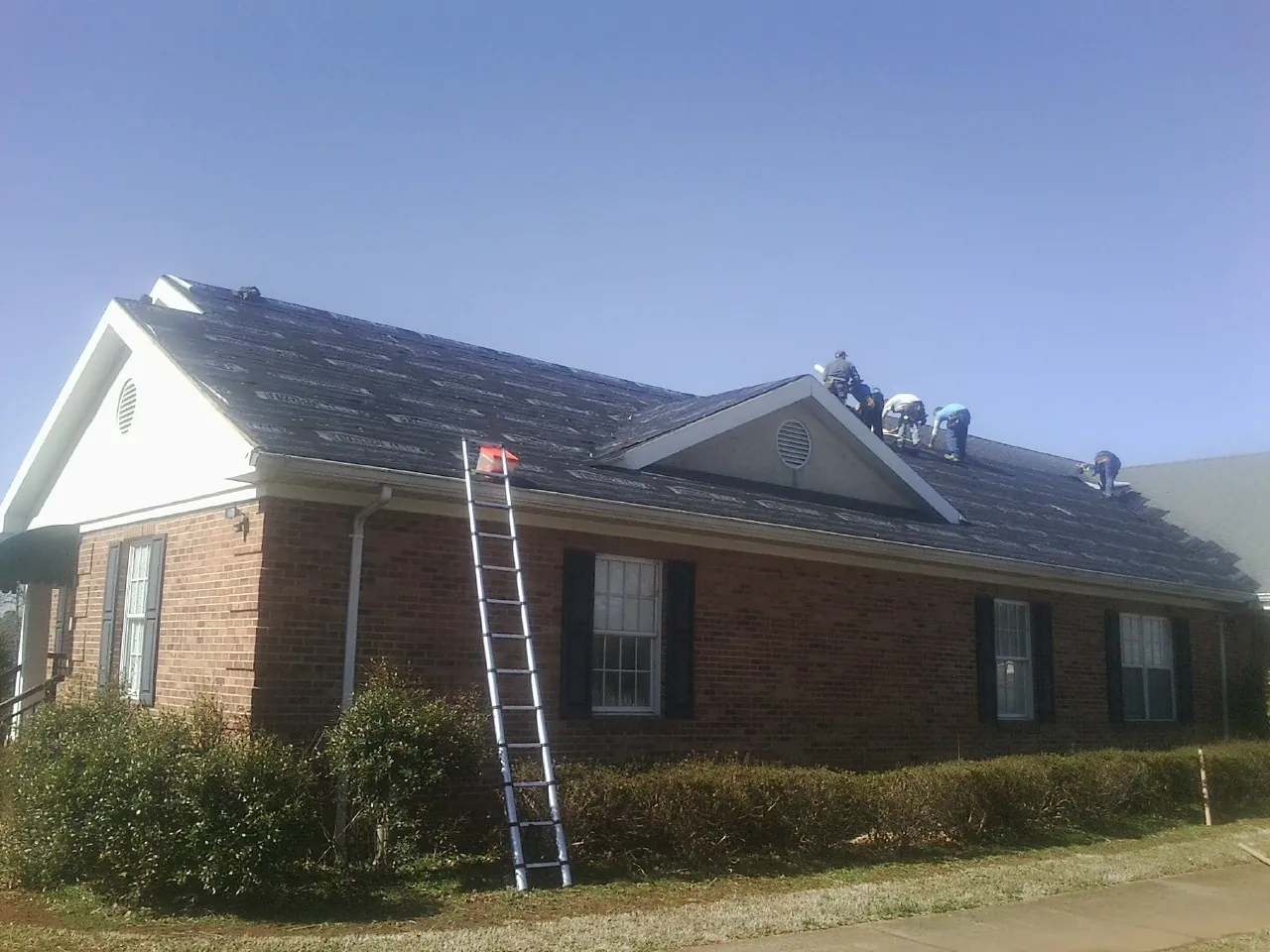 Crew tearing shingles off a brick ranch roof with a ladder set — Metal Roof Repair work by our crew in Kenoza Lake