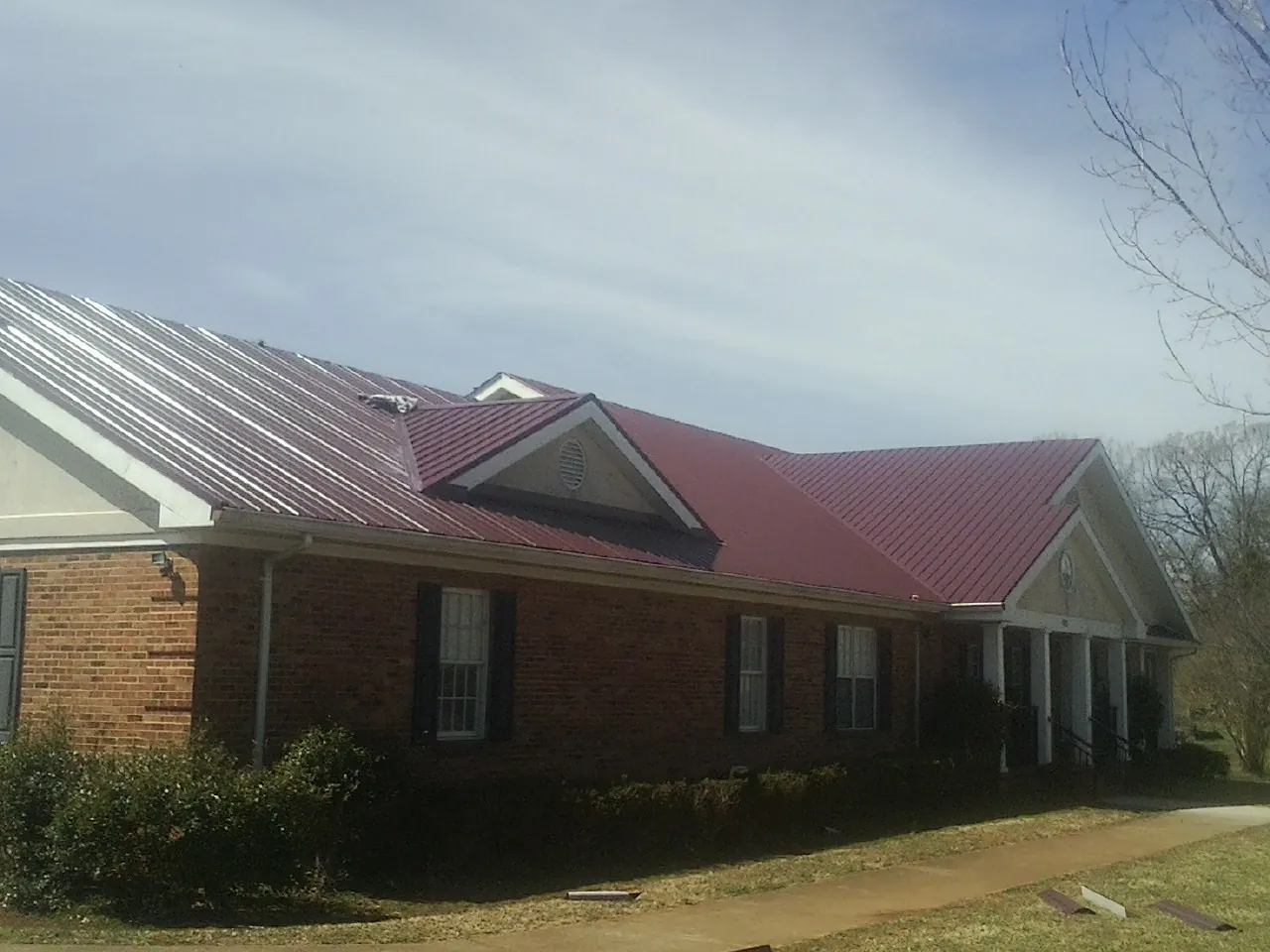 Red metal roof with gabled entries on a long brick building, from a Hail Damage Roof Repair job in Kenoza Lake