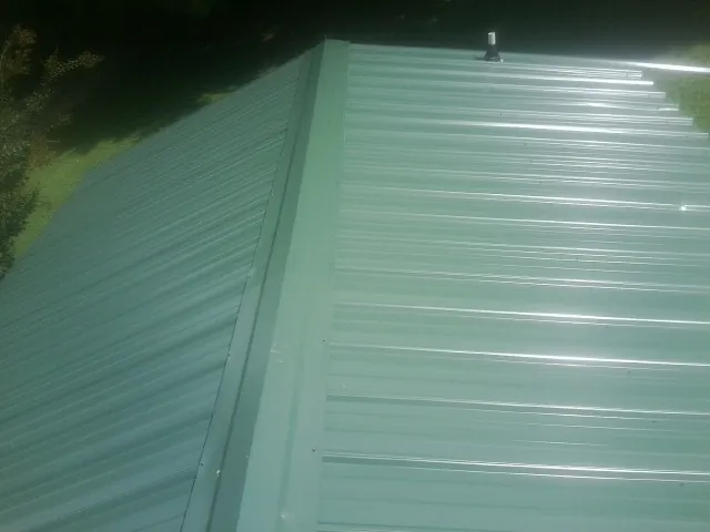 New green metal panels meeting at the ridge of a roof — Flat Roof Repair work by our crew in Kenoza Lake