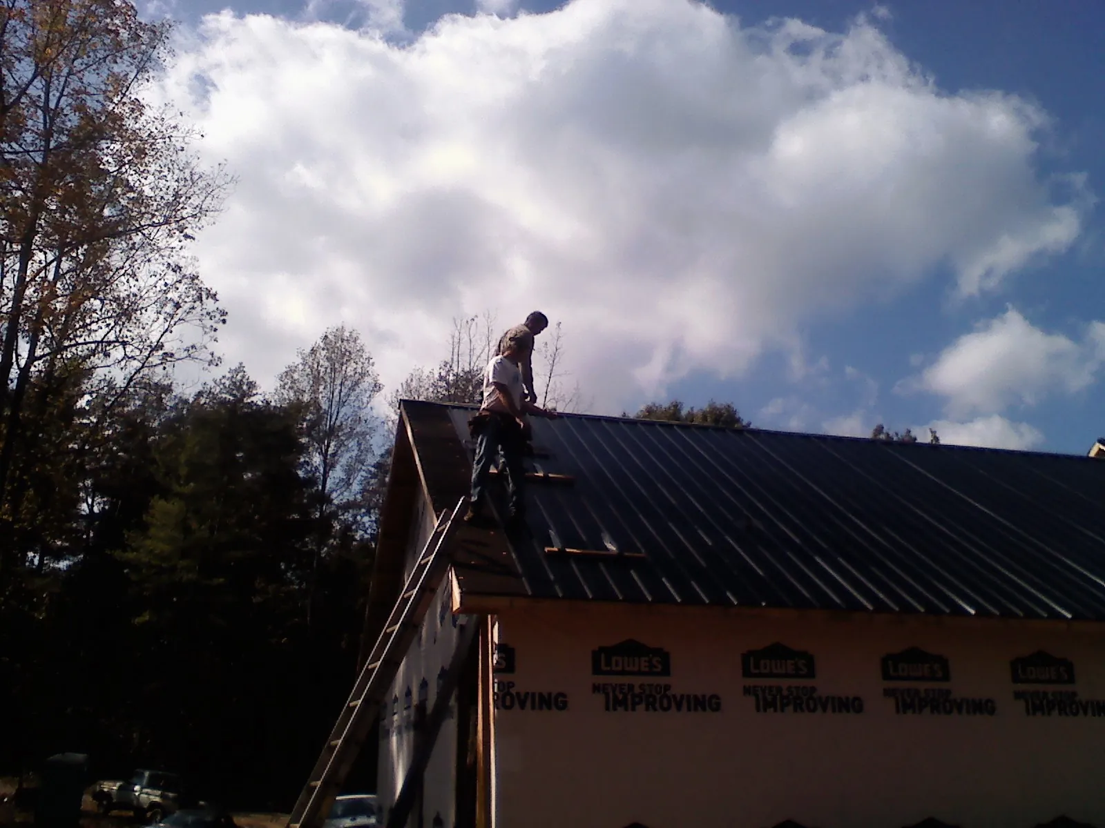 Roofer fastening dark metal panels high against a cloudy sky, from a Roof Inspection job in Kenoza Lake