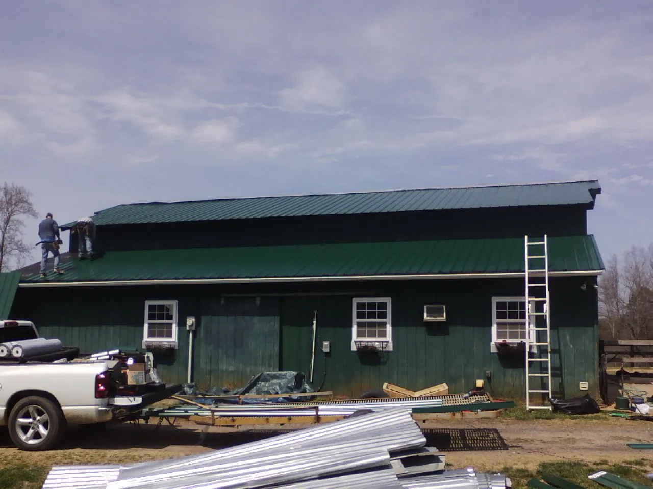 Crew installing green metal roofing on a large green barn in Kenoza Lake
