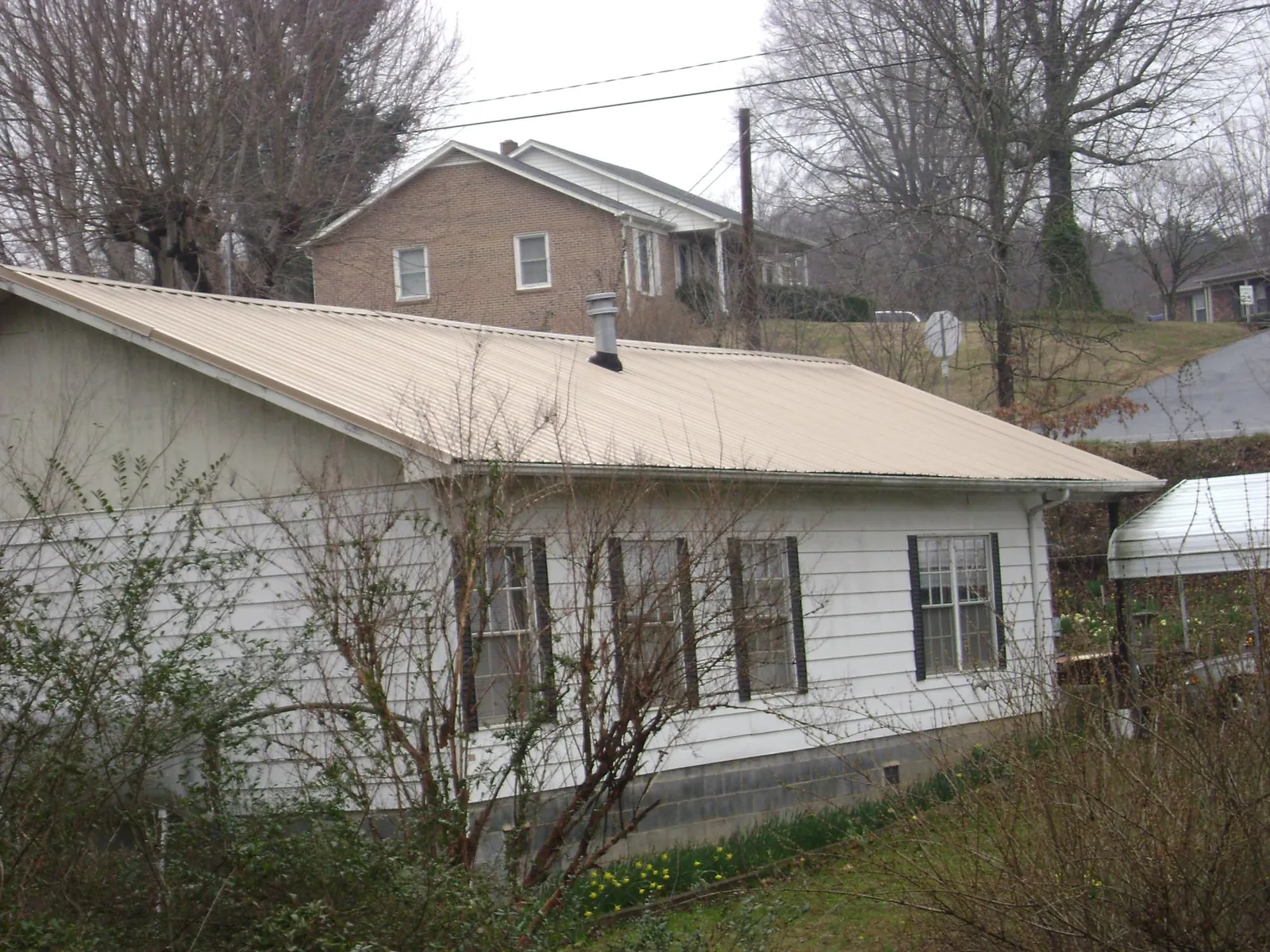 Tan metal roof on a white sided house set into a hillside — Commercial Roofing by Roofing Brothers in Kenoza Lake