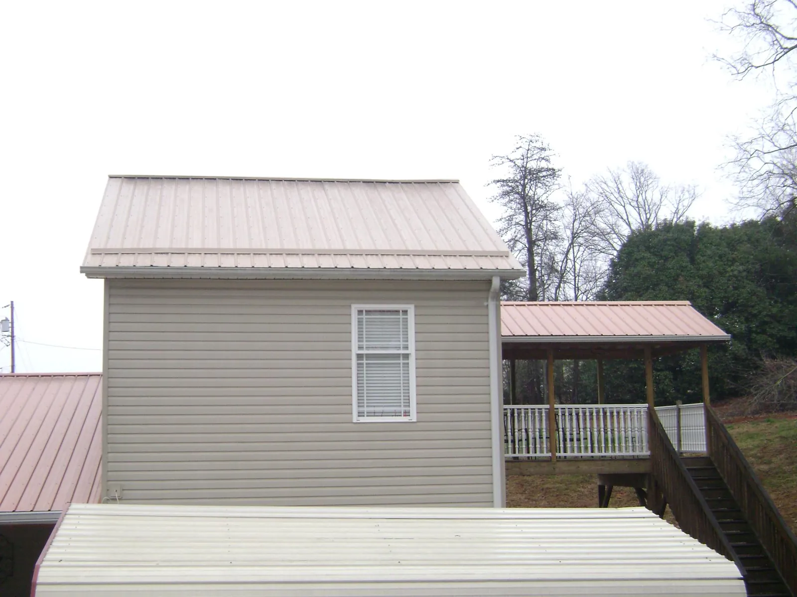 Tan metal roofs on a two story addition and attached porch, from a Roof Replacement job in Kenoza Lake